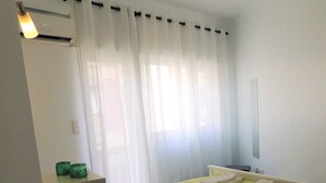A bedroom with a bed, a bedside table, a nightstand, a lamp, and a window with curtains. - RENDEZ VOUS PORTO I (T1) (Paranhos - Porto)