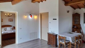 Quarto com teto de madeira, cama com roupa de cama branca, mesa de jantar com cadeiras e um armário de madeira.