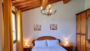 Quarto com cama de madeira, duas mesas de cabeceira com abajures, um candelabro e um guarda-roupa.