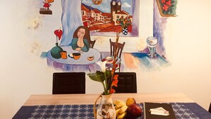 Un'area pranzo con un tavolo apparecchiato per due persone, un vaso di fiori e un piatto di frutta.