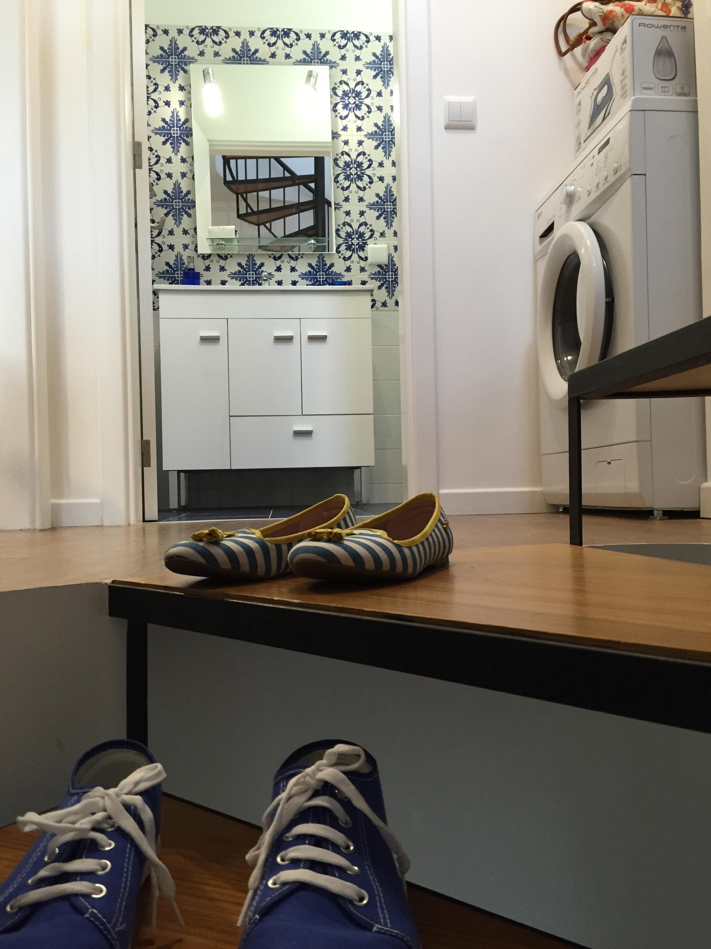 A room with a wooden floor, a white cabinet with drawers, a washing machine, and a pair of shoes on a table.
