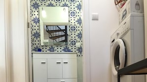 Una stanza con pavimento in legno, un armadietto bianco con cassetti, una lavatrice e un paio di scarpe su un tavolo.
