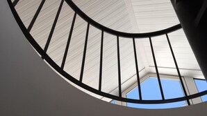 Un elemento architettonico circolare con ringhiera metallica e vista aperta sul cielo attraverso una finestra.