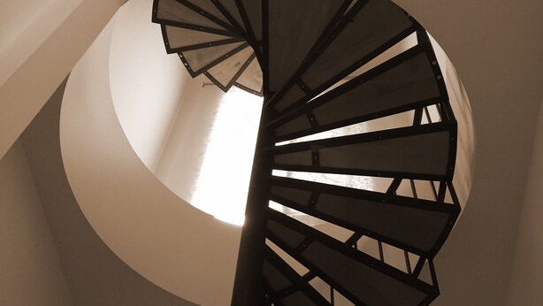 Una scala a chiocciola dal design moderno, caratterizzata da un pilastro centrale e da una serie di gradini che salgono a formare un motivo circolare.