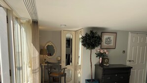 Quarto com escrivaninha, cadeira, cômoda e espelho. Há uma planta em vaso e um quadro na cômoda.