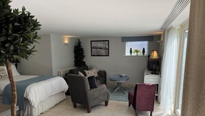 Quarto de hotel com cama, duas poltronas, uma mesinha, janela com vista e árvore de Natal.