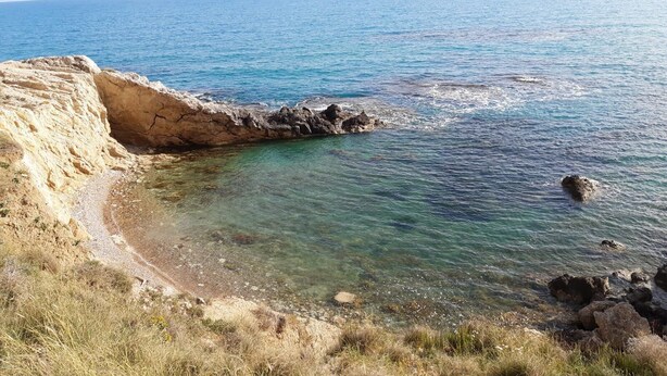 Eine Küstenlandschaft mit klarem Wasser, felsigen Klippen und einem Sandstrand.