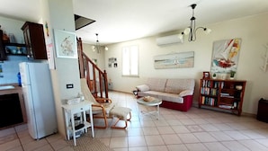 Ein geräumiges Wohnzimmer mit einer Couch, einem kleinen Tisch, einem Bücherregal und einer Treppe, die zu einer anderen Ebene führt.
