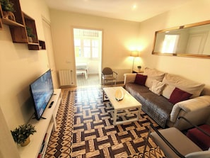 A living room with a sofa, a coffee table, a TV, a patterned rug, and a door leading to another room.