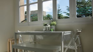 A room with a white table and chairs, a patterned floor, and a window with a view of trees and buildings.