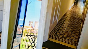 A corridor with patterned floor tiles, a door leading outside, and a view of buildings in the distance.