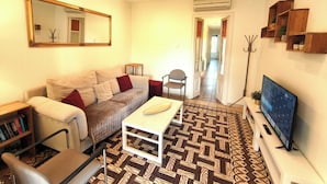 A living room with a sofa, armchair, coffee table, TV, bookshelf, and patterned floor.