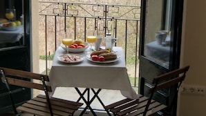 A balcony with a table set for breakfast, a chair, and a view of buildings in the background.