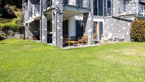 A two-story stone house with a balcony, a small patio with outdoor furniture, and a well-maintained lawn. - Relaxing Oasis: Villa with Private Pool & View (Baveno)