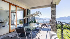 A modern balcony with a glass table and chairs, a potted orchid, and a view of mountains. - Relaxing Oasis: Villa with Private Pool & View (Baveno)