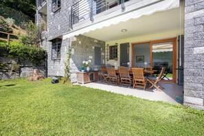 Une maison moderne avec une façade en pierre, un patio couvert agrémenté de meubles en bois et une pelouse bien entretenue.
