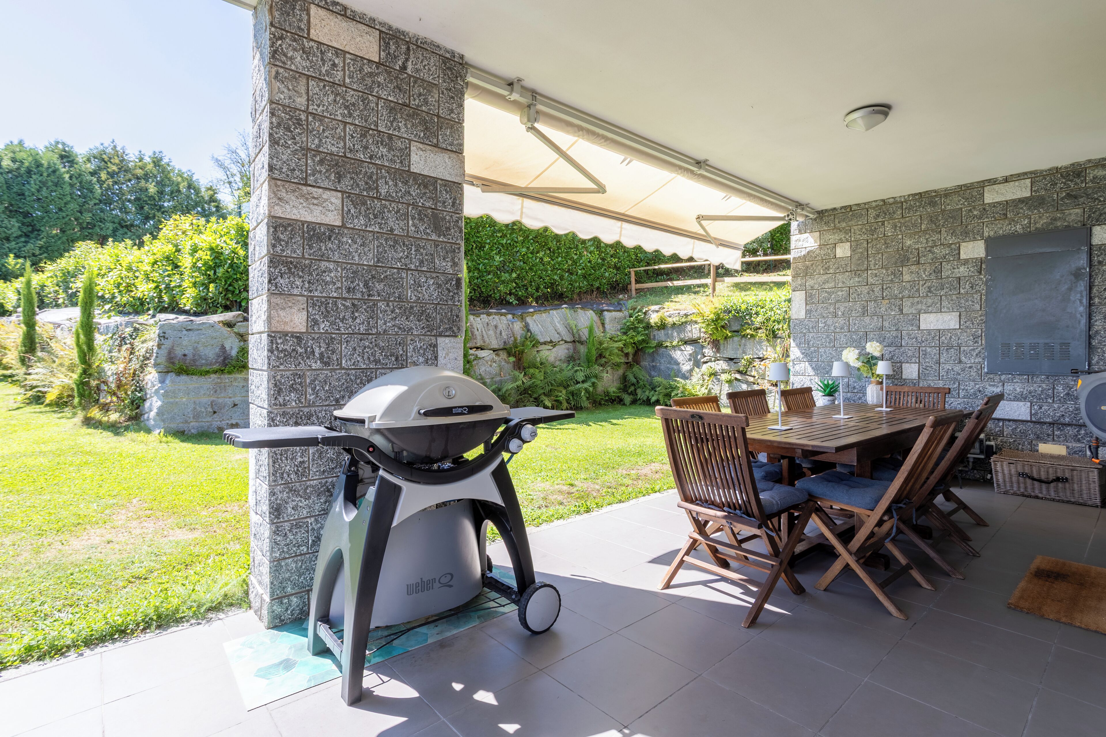 Une terrasse extérieure avec un mur en pierre, un barbecue et un espace repas comprenant des chaises et une table.