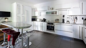 A modern kitchen with white cabinets, stainless steel appliances, and a glass-top dining table with red bar stools. - Relaxing Oasis: Villa with Private Pool & View (Baveno)