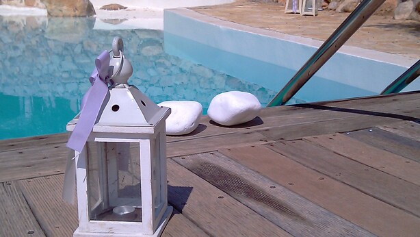 Une terrasse en bois, ornée d’une lanterne blanche et de deux pierres blanches, au bord d’une piscine.