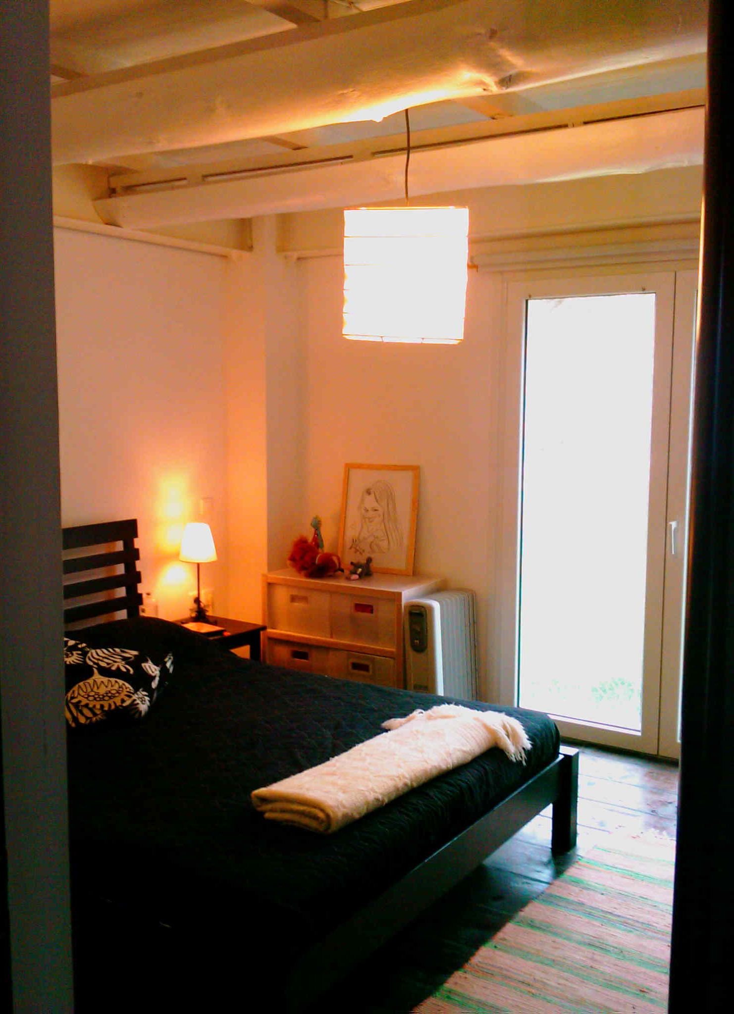 A bedroom with a bed, bedside table, lamp, dresser, and a window.