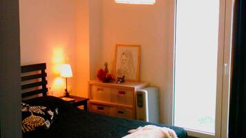A bedroom with a bed, bedside table, lamp, dresser, and a window.