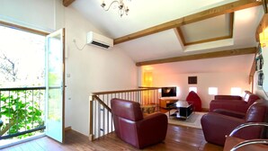 A spacious living room with wooden flooring, a staircase, and a balcony with a view of greenery. - Gîte with pool, grounds, air-conditioning for peaceful family holidays in Landes (Sainte-Colombe)