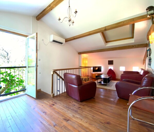 A spacious living room with wooden flooring, a staircase, and a balcony with a view of greenery. - Gîte with pool, grounds, air-conditioning for peaceful family holidays in Landes (Sainte-Colombe)