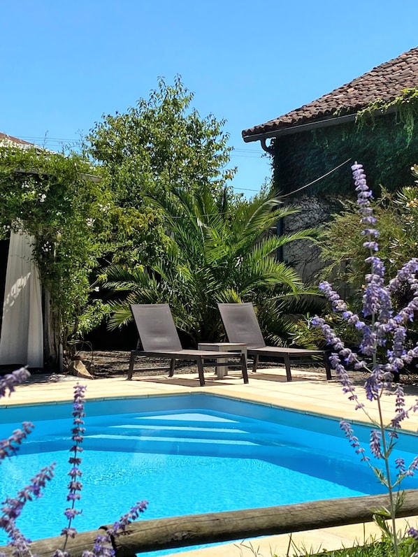 A swimming pool with two lounge chairs, surrounded by lush greenery and a building with a tiled roof. - Gîte with pool, grounds, air-conditioning for peaceful family holidays in Landes (Sainte-Colombe)