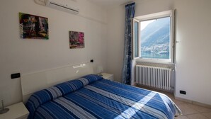 A bedroom with a bed, a radiator, a window with a view of a town and mountains, and two wall art pieces. - COLOR WITH PANORAMA AND RENOVATED PARKING (Careno)