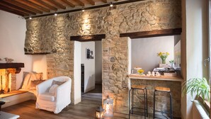A cozy interior with stone walls, a wooden ceiling, a white armchair, a bar area, and a lantern.