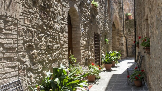 A narrow stone alley with potted plants and benches.