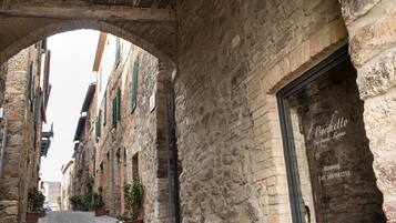 Une rue étroite bordée d’immeubles en pierre, un arc de triomphe et une porte sur laquelle est apposée une enseigne indiquant « M. Borghetto ».
