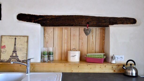 A kitchen with a wooden shelf, a white kettle, a pink dish rack, and a Bixvils container.
