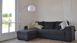 A modern living room with a sectional sofa, a floor lamp, and a large window providing a view of greenery outside.