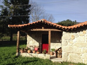 Un bâtiment en pierre avec un toit en tuiles, une porte en bois et des plantes en pot disposées au sol.