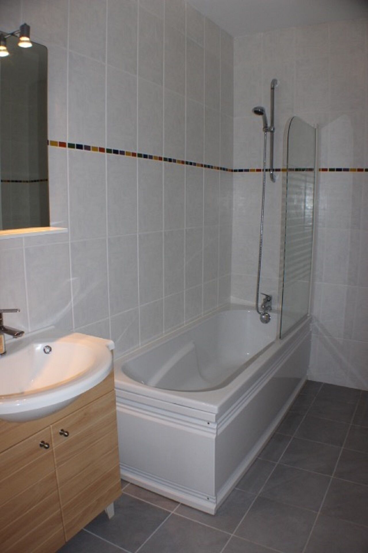 A modern bathroom with a white bathtub, a wooden vanity with a sink, and a glass-enclosed shower area.