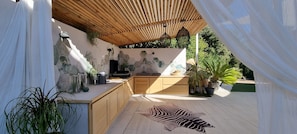 Un espace cuisine extérieur doté de meubles de rangement en bois, d’un tapis à motifs zébrés et de plantes en pot.