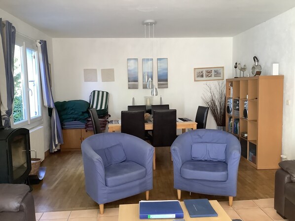 A living room with two blue armchairs, a wooden dining table with chairs, a bookshelf, and a fireplace.