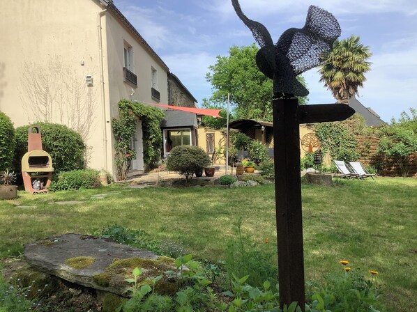 Un jardin agrémenté d’un barbecue extérieur rustique, d’un panneau indicateur en bois et d’une maison au toit rouge.