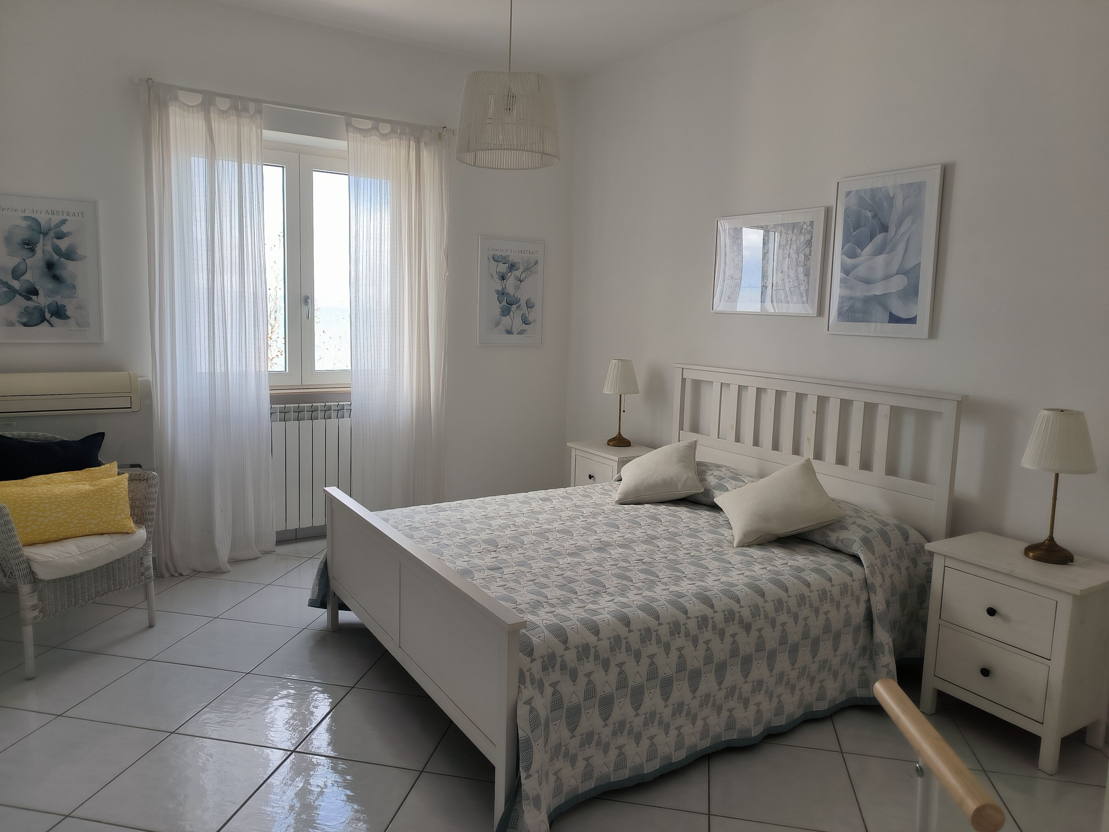 Un dormitorio con una cama, mesitas de noche, una silla y una ventana con cortinas.