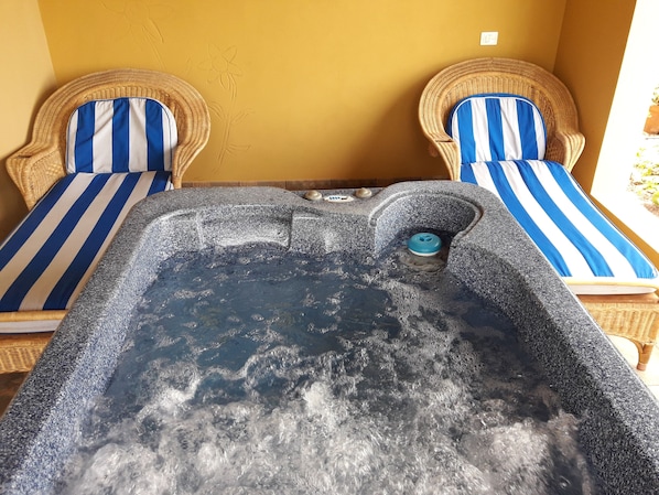 Un bain à remous avec deux fauteuils en osier, chacun agrémenté d’un coussin à rayures bleues et blanches, le tout adossé à un mur jaune.
