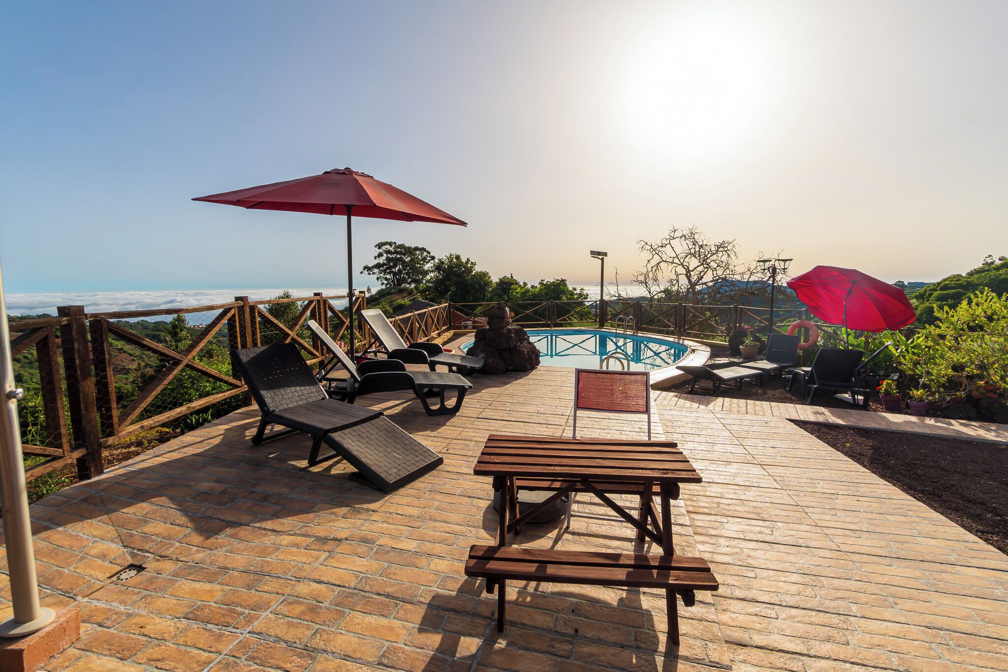 A wooden deck with lounge chairs and a table, overlooking a pool and a scenic view.