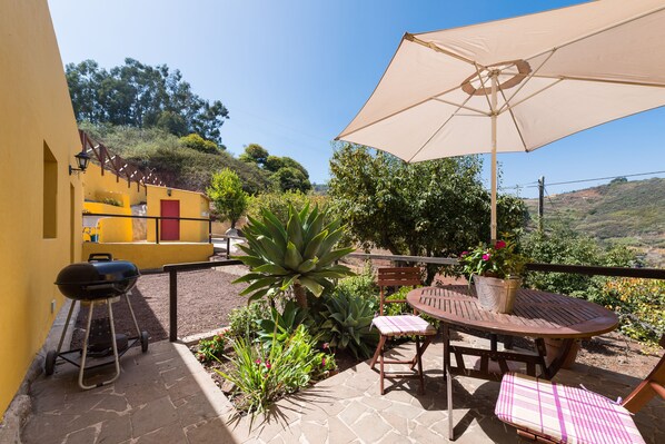 A patio with a round table, chairs, a grill, and an umbrella.