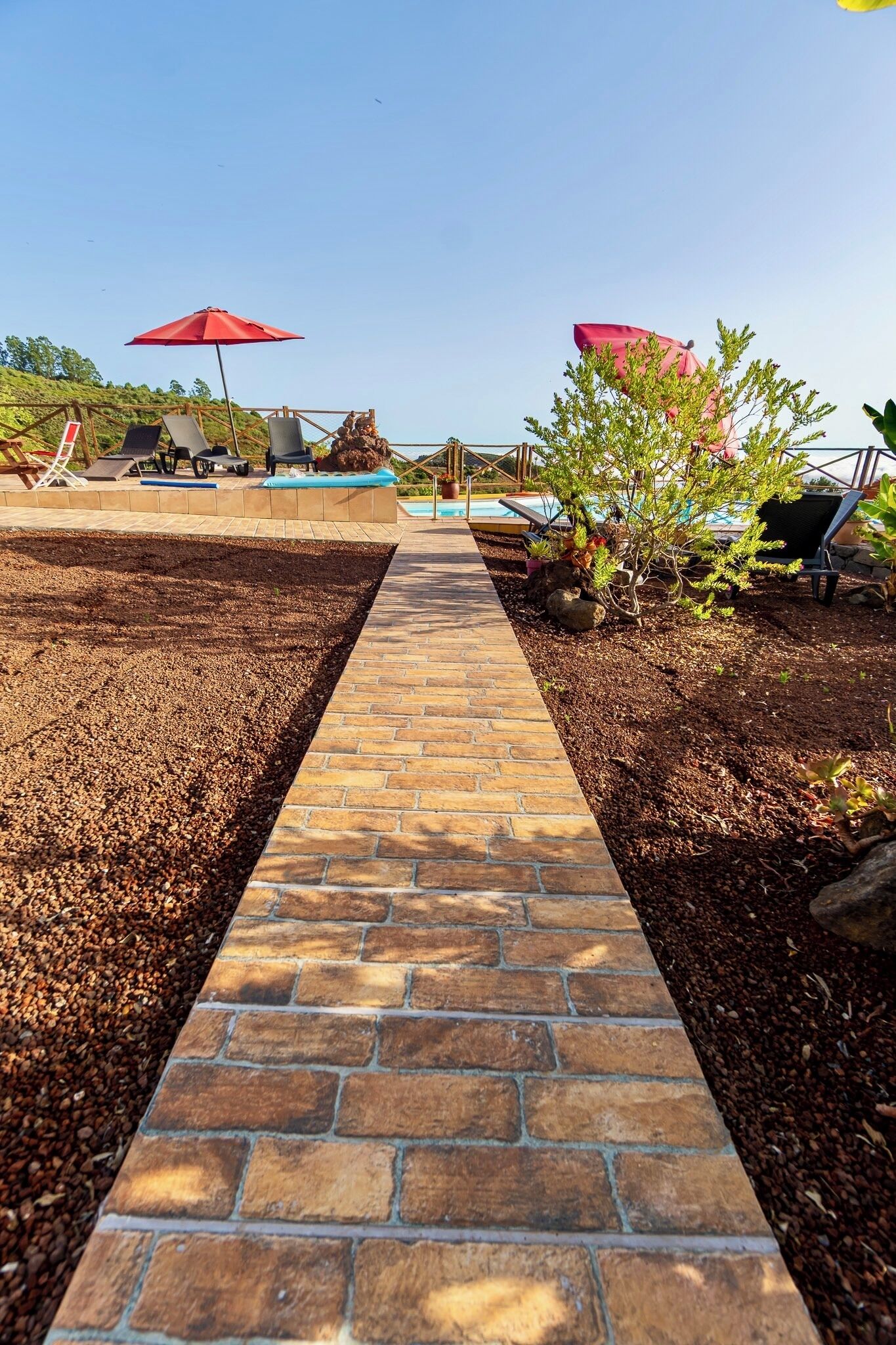 A pathway leading to a pool area with lounge chairs and umbrellas.