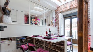 Un espace repas moderne avec une table blanche dressée pour deux personnes, entourée d’étagères et d’un mur en briques.