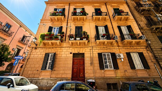 A multi-story building with balconies, a red door, and parked cars.