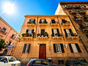 A multi-story building with balconies, a red door, and parked cars. - Apartment Via Fiume (Palermo)