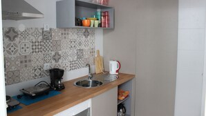 Ett kök med en diskho i rostfritt stål, en kaffebryggare och ett urval av färgglada koppar och skålar på en hylla.