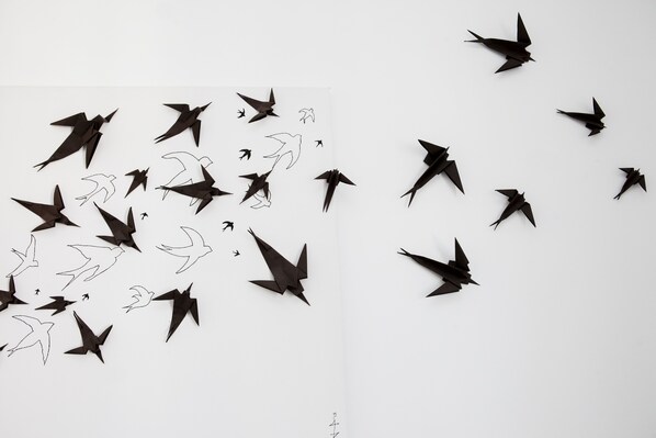 A white wall with multiple black origami birds scattered across it.