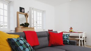 Ett modernt vardagsrum med en grå soffa, röda och flerfärgade kuddar, ett träbord och en matplats med ett vitt bord och stolar.
